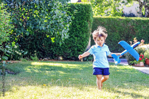 Cute little boy with funny flying hair and toy plane in his hand running barefoot on grass in garden. Happy carefree childhood, summer lifestyle. © Tetiana Soares