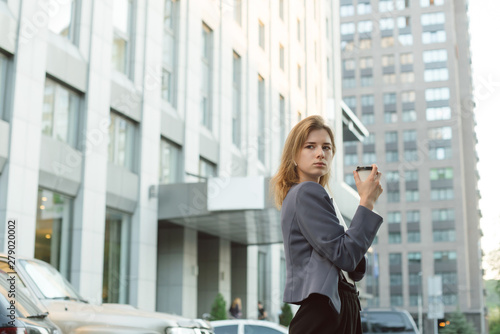 Prosperous female entrepreneur in formal wear looking back seriously while holding coffee cup walking on street  busy businesswoman satisfied with successful news after work in the business center.