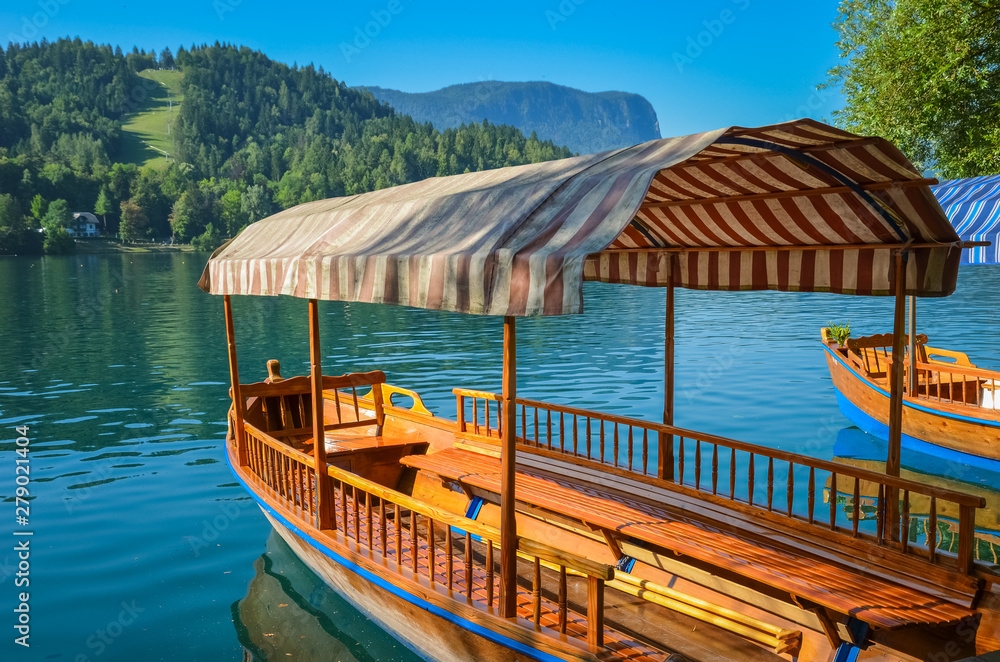 Beautiful wooden boat on famous Bled Lake in Slovenia. Bled Lake, known for its castle and island, is popular travel destination. Tourist boats are used for summer sightseeing tours on the blue lake Beautiful wooden boat on famous Bled Lake in Slovenia. Bled Lake, known for its castle and island, is popular travel destination. Tourist boats are used for summer sightseeing tours on the blue lake