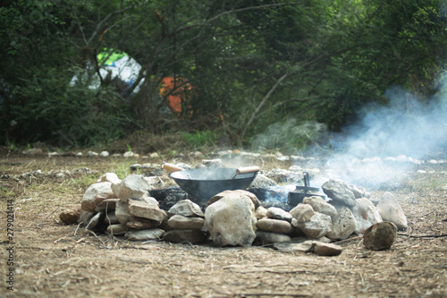 Wok pan and tea pot on a heavily smoking campfire surrounded with stones in a natural environment.