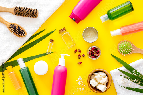 Cosmetic for hair treatment with shampoo, conditioner, styling, oil, comb on yellow background top view pattern