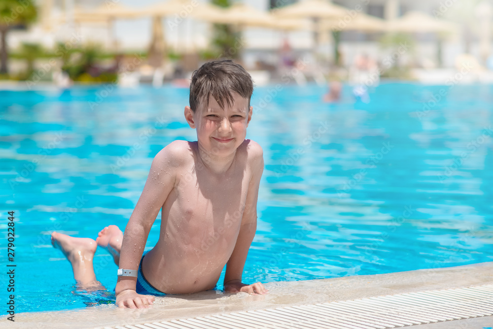 Smiling European boy on side of swimming pool at resort on summer.