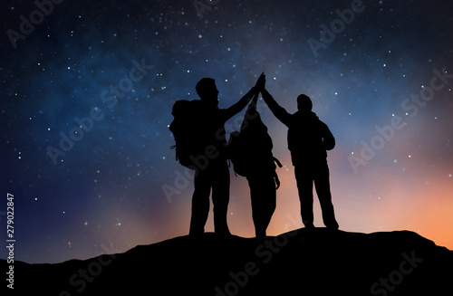 travel, hike and success concept - group of travelers or friends making high five gesture on edge of mountain over starry night sky or space background