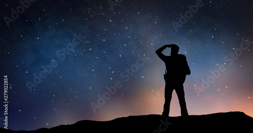 travel, tourism, hike and people concept - silhouette of traveler standing on edge and looking far away over starry night sky or space background