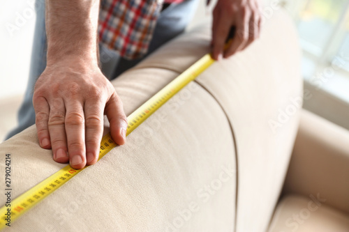 Man measuring beige sofa  closeup. Construction tool
