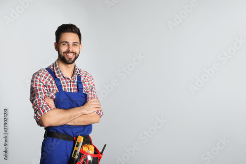 Portrait of construction worker with tool belt on light background. Space for text photo
