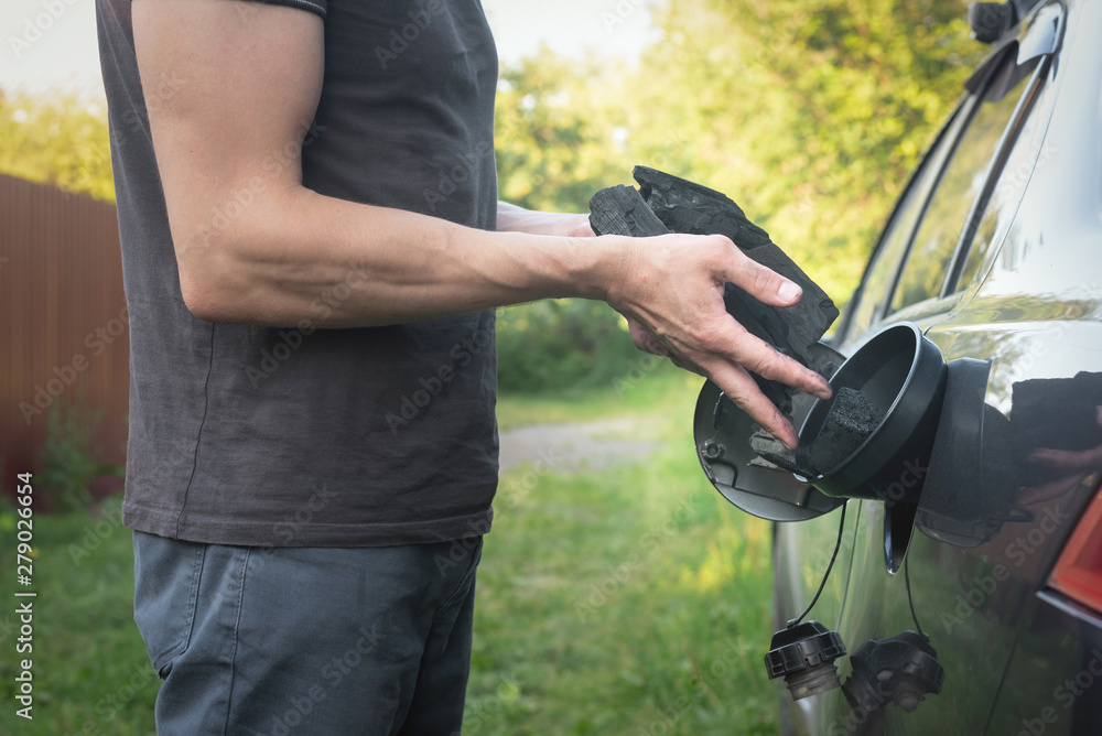 Expensive gasoline. Lack of money for petrol. Driver drops the coal in the gas tank of the car. Increase in gasoline prices and search for alternative fuels concept.