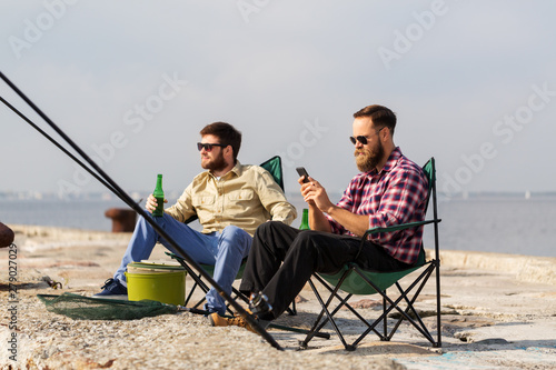 leisure and people concept - male friends with smartphone fishing and drinking beer