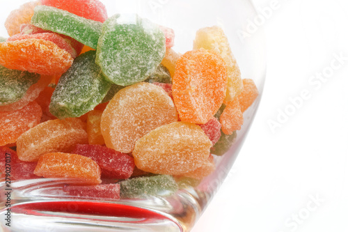 Multicolored candied sugar fruits are in a glass jar on a white background. Place to sign