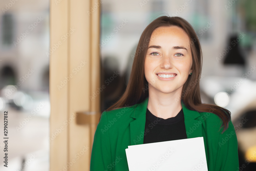 Portrait of a beautiful girl with long hair in a green jacket with documents in hand, girl smiling. Portrait of a beautiful girl with long hair in a green jacket with documents in hand, girl smiling.