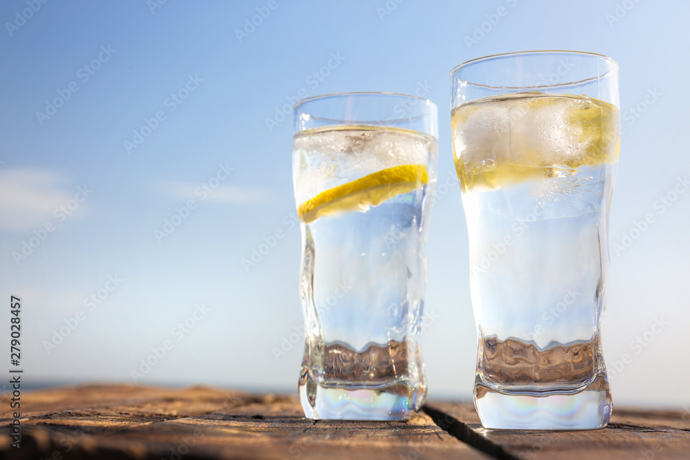 Wooden table with glasses of refreshing lemon drink on hot summer day outdoors, space for text Wooden table with glasses of refreshing lemon drink on hot summer day outdoors, space for text