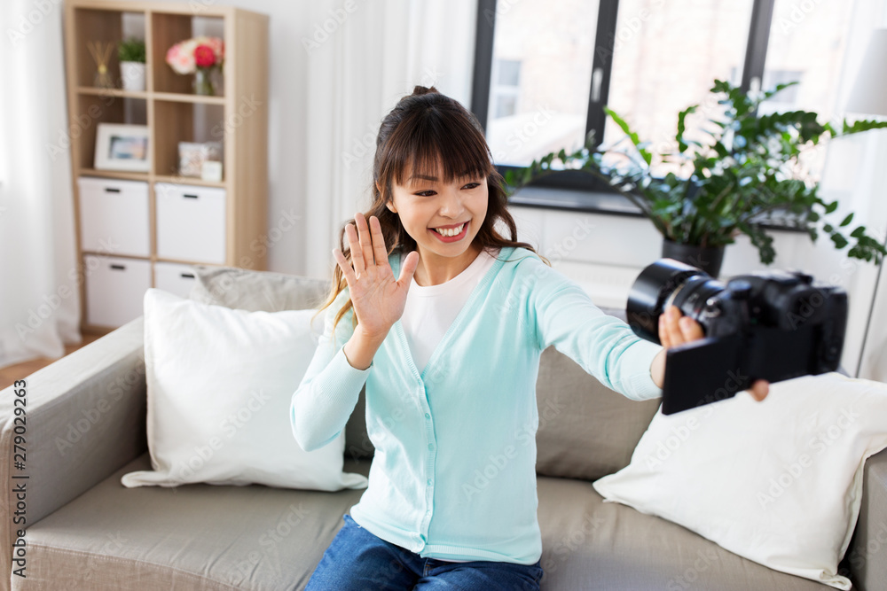 blogging, videoblog and technology concept - asian woman or blogger with camera recording video blog or taking selfie and waving hand at home blogging, videoblog and technology concept - asian woman or blogger with camera recording video blog or taking selfie and waving hand at home
