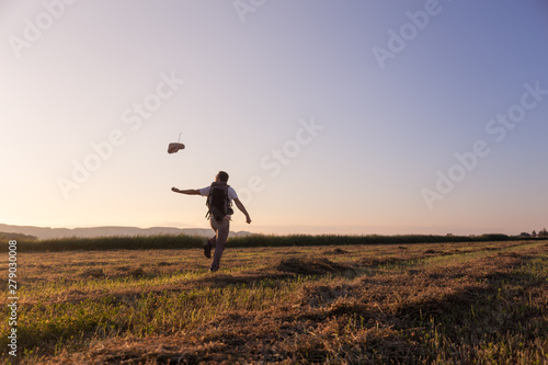 backpacker traveler walking at sunrise and throwing hat in the wind