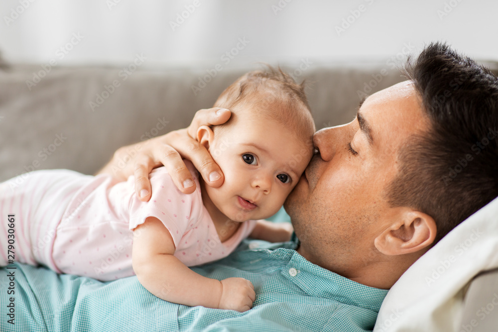 family, parenthood and fatherhood concept - middle aged father kissing little baby daughter lying on sofa at home - obrazy, fototapety, plakaty 