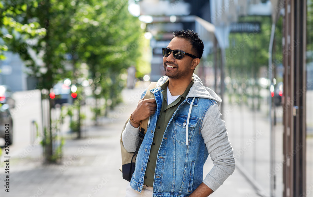 travel, tourism and lifestyle concept - smiling indian man in sunglasses with backpack on city street