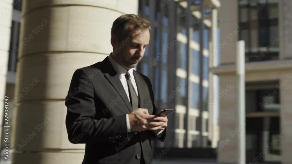 Panning waist up shot of determined middle aged businessman in formal wear typing and sending text message on cell phone on the move. Man walking down street on sunny day confidently Panning waist up shot of determined middle aged businessman in formal wear typing and sending text message on cell phone on the move. Man walking down street on sunny day confidently