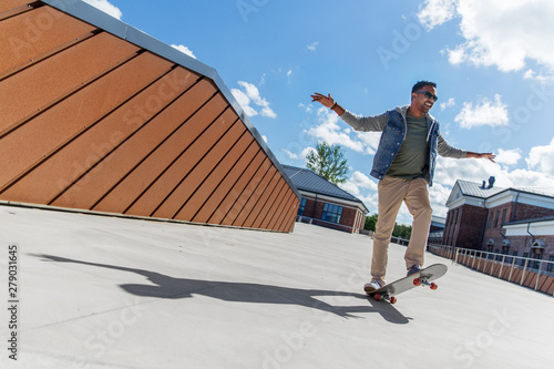 people and leisure concept - smiling indian man doing trick on skateboard on roof top