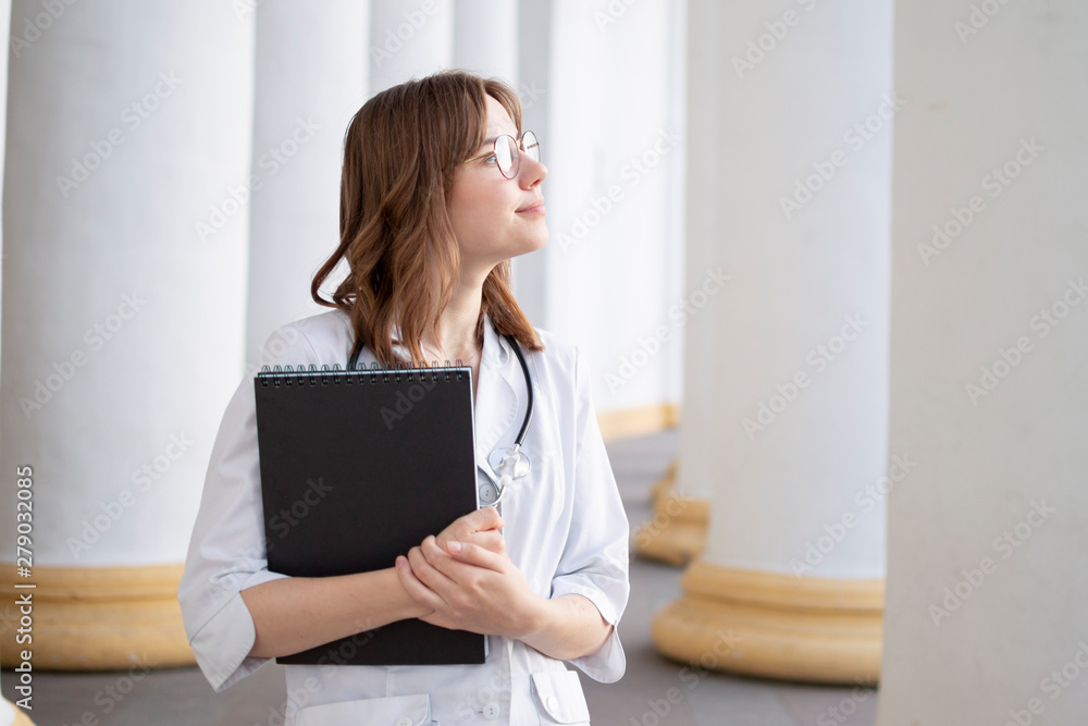 young girl student at a medical university standing in the corridor, portrait of an attractive nurse near the hospital, happy female doctor with a stethoscope in uniform