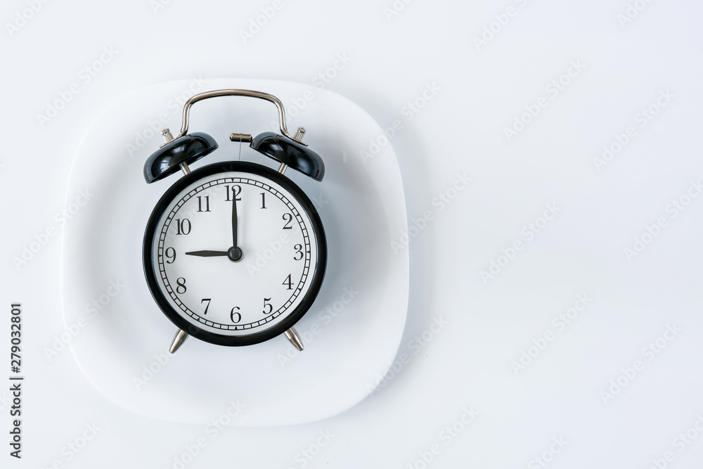 Black alarm clock in white plate with fork on the table. Time to eat ...