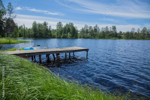 Simple wooden jetty by the lake with high green grass in the foreground