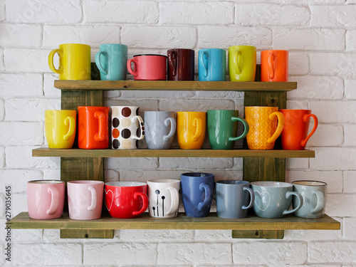 Set of multicolored coffee cups on a shelf on the white brick wall in cozy city cafe