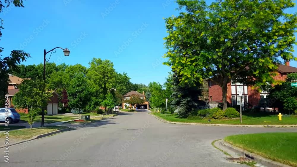 Driving Residential City Road With Lush Trees During Summer Day. Driver Point of View POV Along Beautiful Sunny Suburban Street. Driving Residential City Road With Lush Trees During Summer Day. Driver Point of View POV Along Beautiful Sunny Suburban Street.