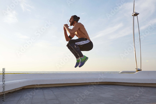 Young bearded jumping man with fit athletic body,doing morning exercises and listening music on headphones, has muscular body shape.