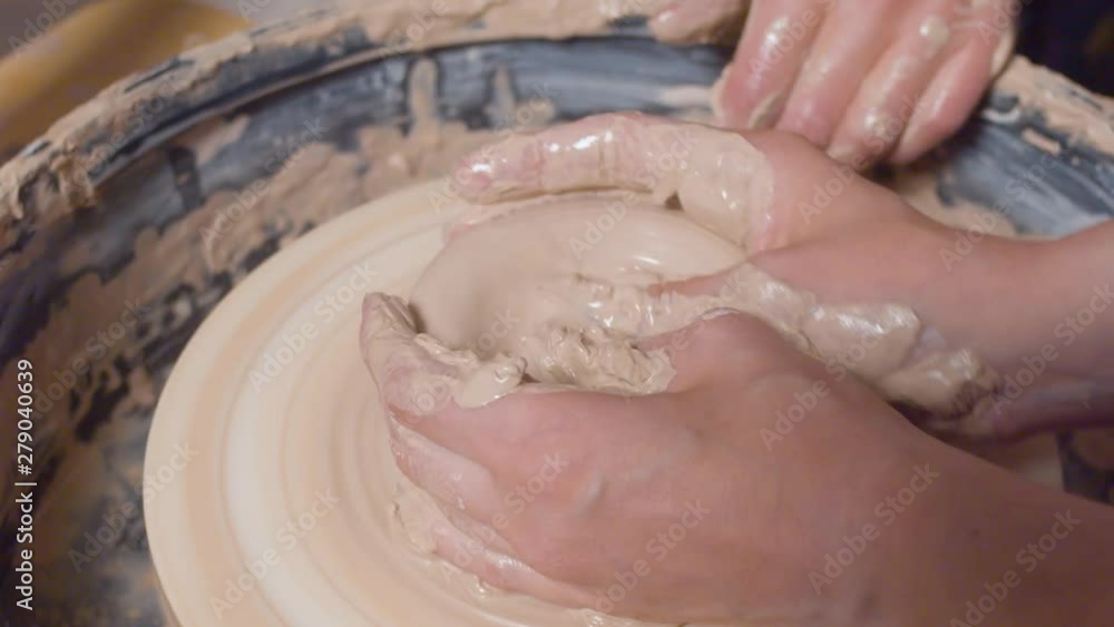 Woman's hands making a pot on a potter's wheel. Close up, top view Woman's hands making a pot on a potter's wheel. Close up, top view