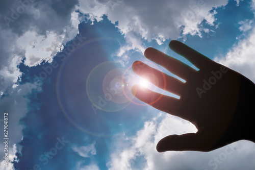 hand silhouette against the cloudy sky with lens flare