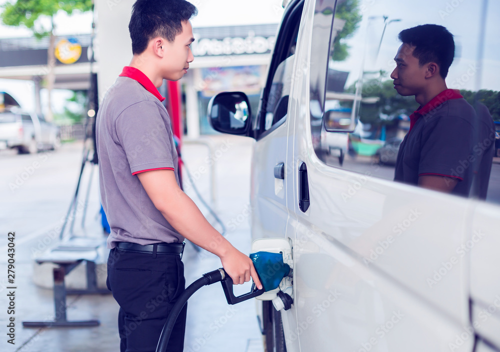 Selective focus to Asian staff is providing fueling services to white van in gas station. Hand refilling the white van with fuel at the gas station. Oil and gas energy. Selective focus to Asian staff is providing fueling services to white van in gas station. Hand refilling the white van with fuel at the gas station. Oil and gas energy.