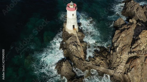 View from above, stunning aerial view of an old and beautiful lighthouse located on a rocky coast bathed by a rough sea. Faro di Capo Ferro, Porto Cervo, Sardinia, Italy.