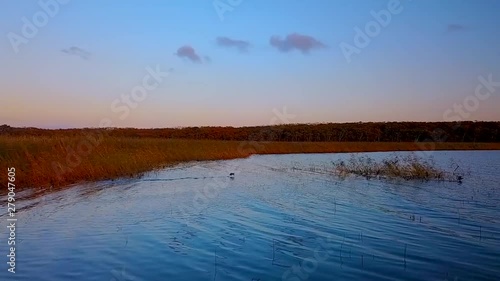 Flying above beautiful lake Blagodatnoye surrounded with green forests and mountains on the background. Wild ducks take off from the water against the backdrop of a beautiful sunset. photo