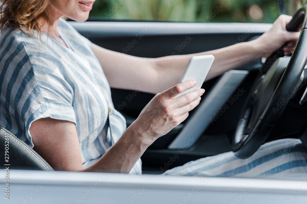cropped view of woman holding steering wheel and using smartphone in car