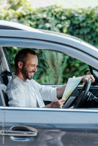 selective focus of happy driver sitting in car and looking at map