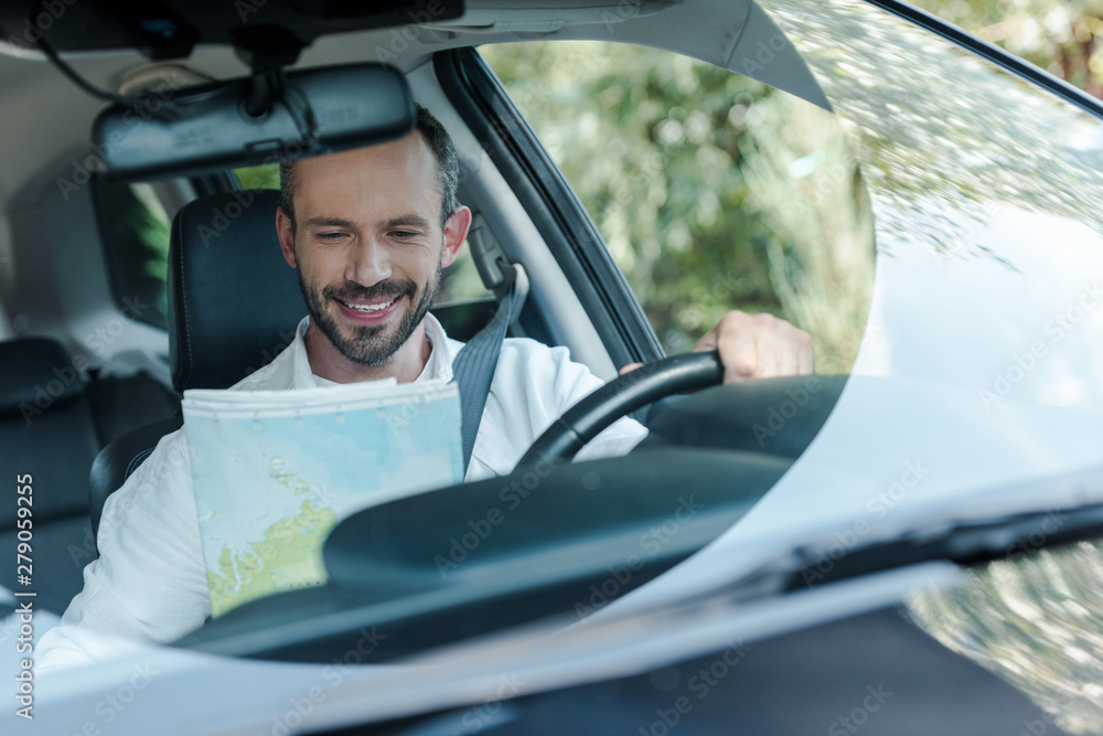 selective focus of happy man driving car and looking at map