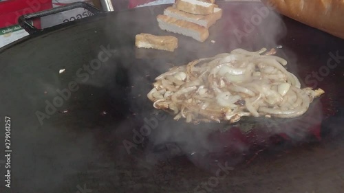 Close up of Hand Cook frying onion and tofu on hot flat pot. Kitchen tongs move the food on the tawa pan. Typical asian street food recipe for lao sandwich. photo