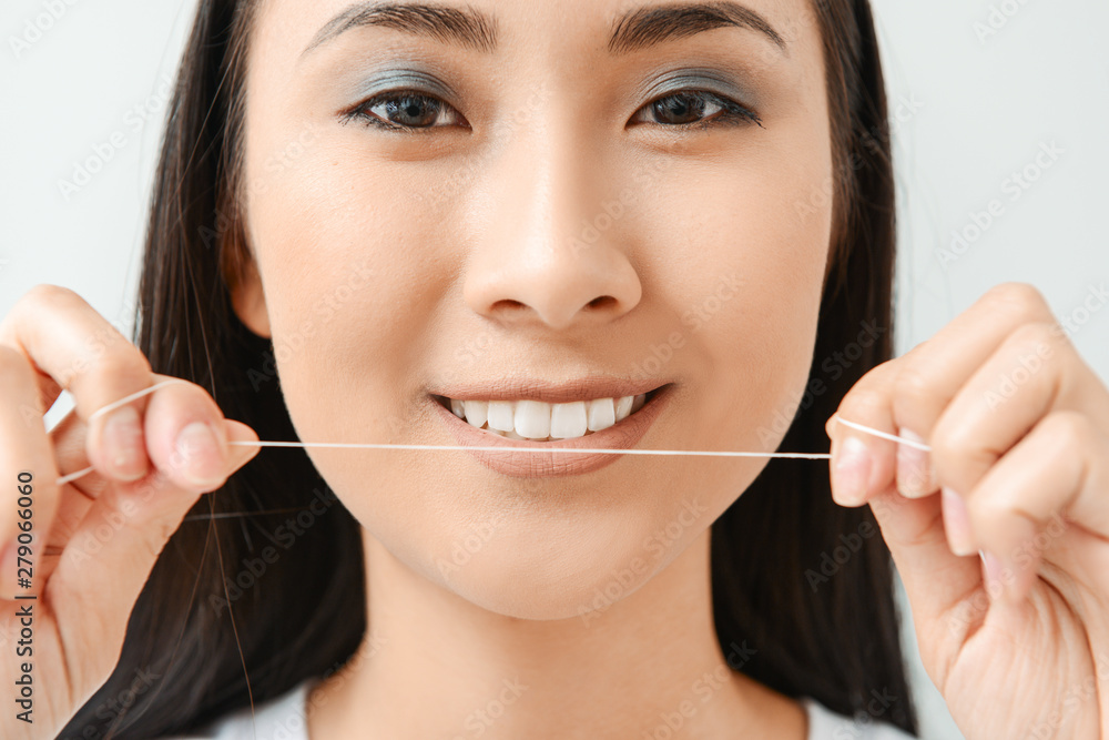 Beautiful Asian woman with dental floss on light background, closeup Beautiful Asian woman with dental floss on light background, closeup