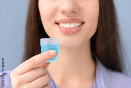 Beautiful woman with cup of mouthwash on color background, closeup