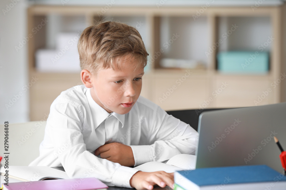 Cute little schoolboy with laptop doing lessons in classroom Cute little schoolboy with laptop doing lessons in classroom