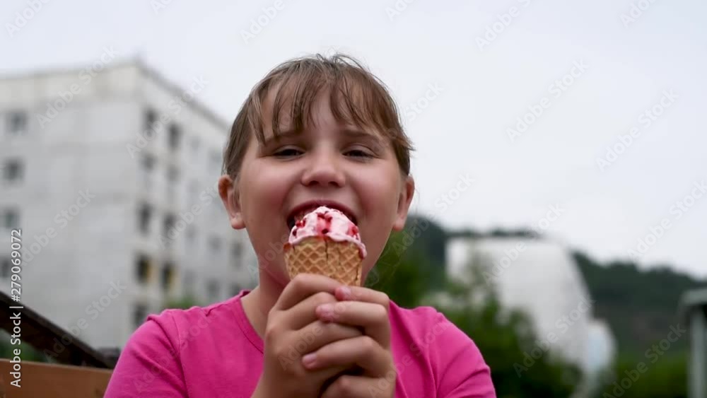 The girlie enjoys a delicious ice cream on a hot day . Girlie eating strawberry ice cream with chocolate chips, while walking 