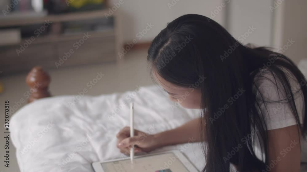 Happy young Asian woman using digital tablet drawing with a stylus pen graphic on bedroom at home. Happy young Asian woman using digital tablet drawing with a stylus pen graphic on bedroom at home.