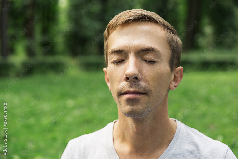 Portrait of the pacified face of a young attractive man with his eyes closed against the background of green foliage. Portrait of the pacified face of a young attractive man with his eyes closed against the background of green foliage.