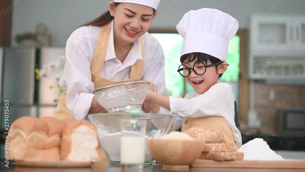 Cute little Asian boy and beautiful mother sifting dough flour with sifter sieve colander in home kitchen on table for prepare to baking bakery and cake. Thai kids playing with flour as chef funny Cute little Asian boy and beautiful mother sifting dough flour with sifter sieve colander in home kitchen on table for prepare to baking bakery and cake. Thai kids playing with flour as chef funny