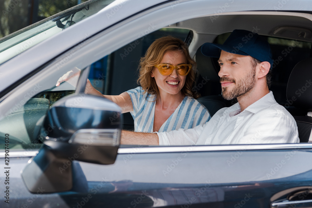 selective focus of happy woman in yellow sunglasses looking at bearded man driving car