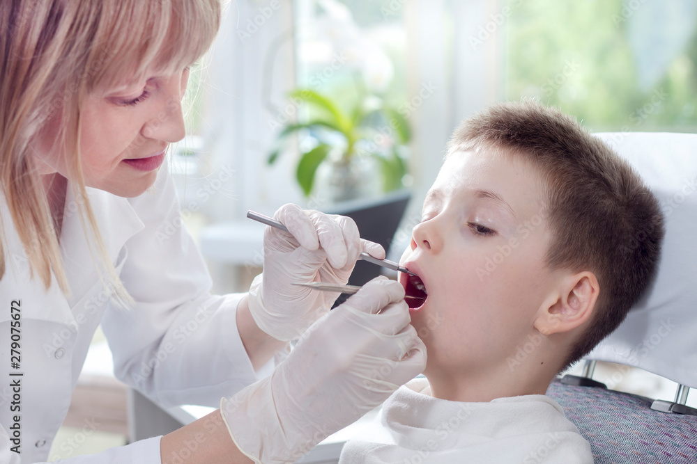 Pani doktor stomatolog w białym fartuchu i jednorazowych rękawiczkach sprawdza stan uzębienia chłopca w wieku szkolnym.