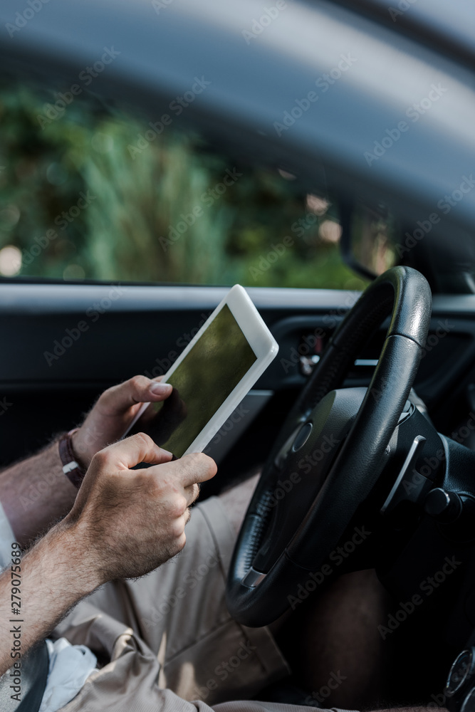 cropped view of man holding digital tablet and sitting in car