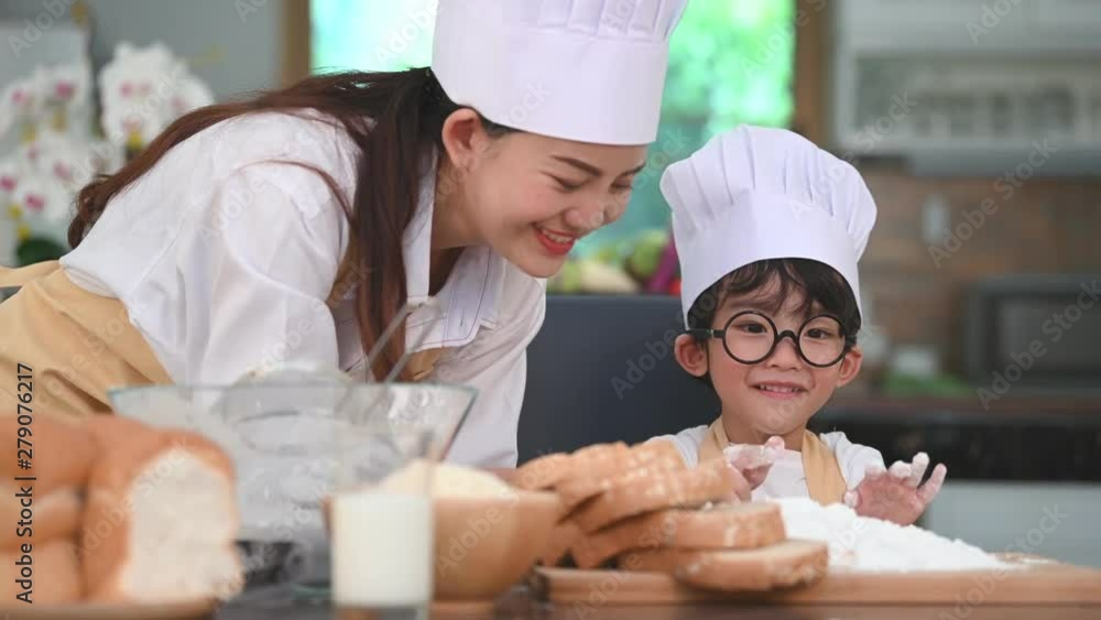 Cute little Asian boy with eyeglasses, chef hat and apron enjoy painting his mother face with dough flour bakery in home kitchen funny. Homemade food. Education and learning concept. Emotion portrait Cute little Asian boy with eyeglasses, chef hat and apron enjoy painting his mother face with dough flour bakery in home kitchen funny. Homemade food. Education and learning concept. Emotion portrait