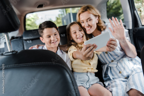 selective focus of happy family taking selfie on smartphone in car