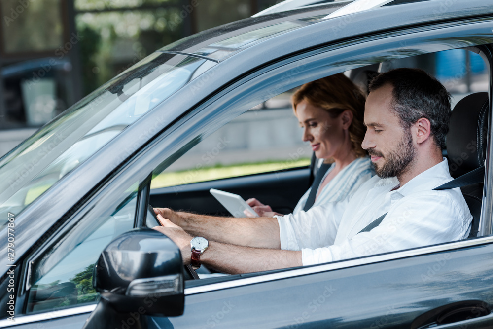 selective focus of man driving car while woman using digital tablet