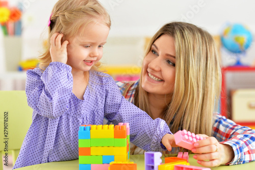Cute little girl and her mother playing colorful plastic blocks